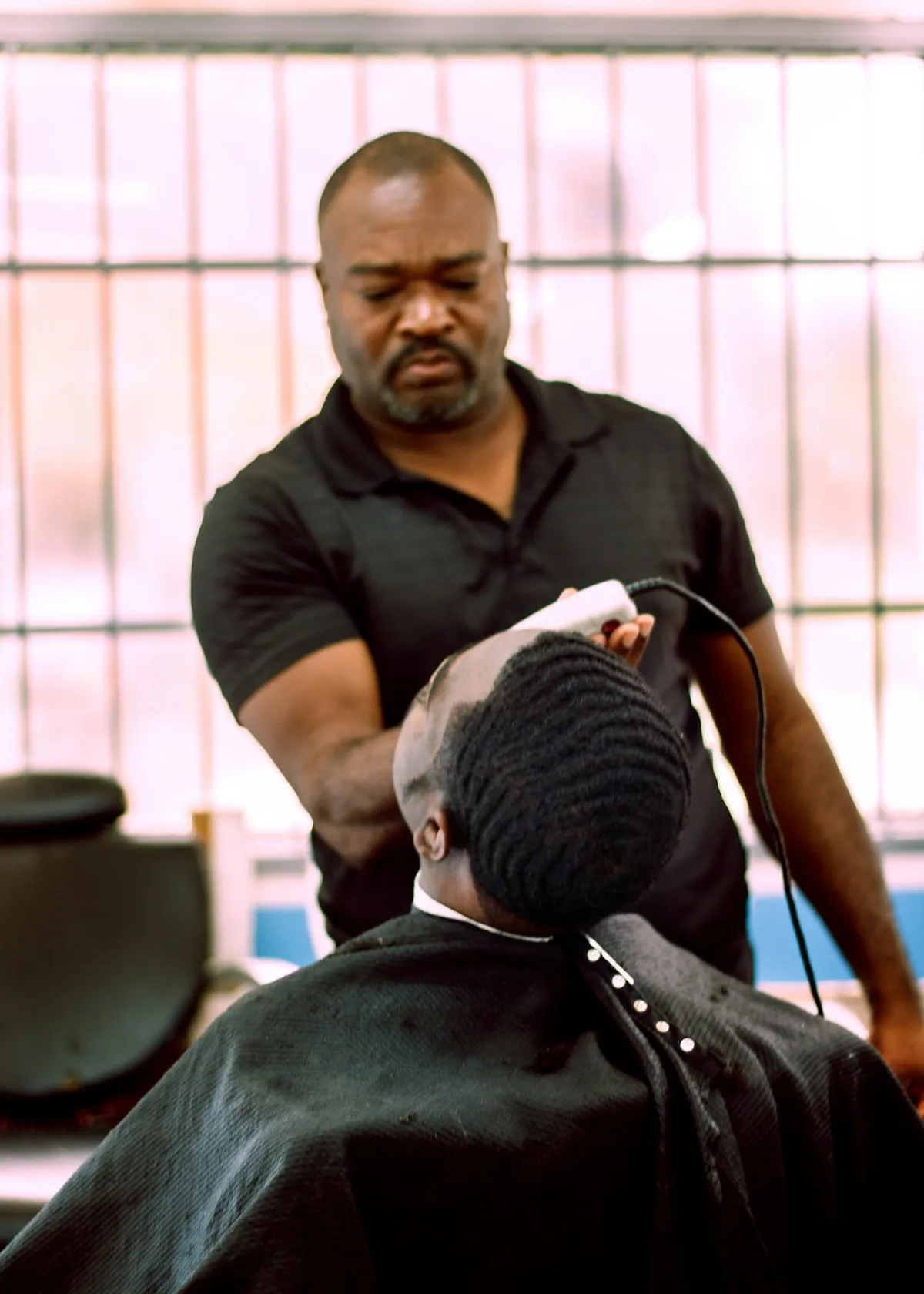 Barbier souriant réalisant une coupe à la tondeuse dans un salon de barbier