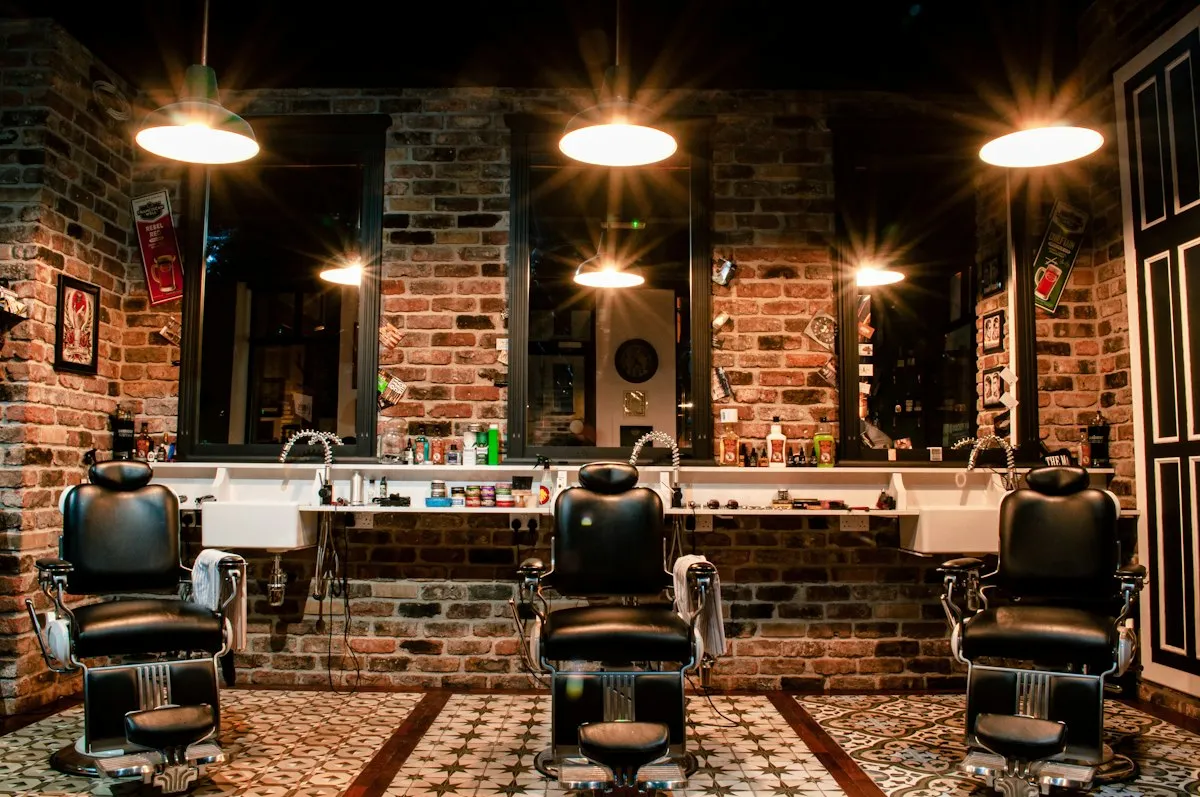 Fauteuil de barbier en cuir devant un mur de briques, sous une suspension lumineuse